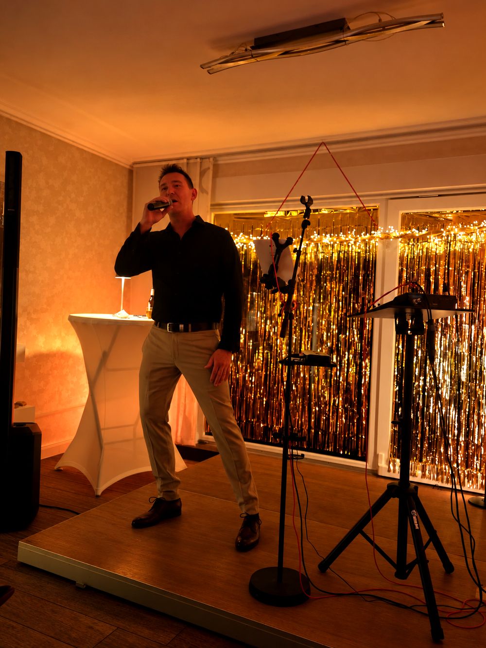 Kay Schmeller singt bei einer Feier vor goldenem Vorhang